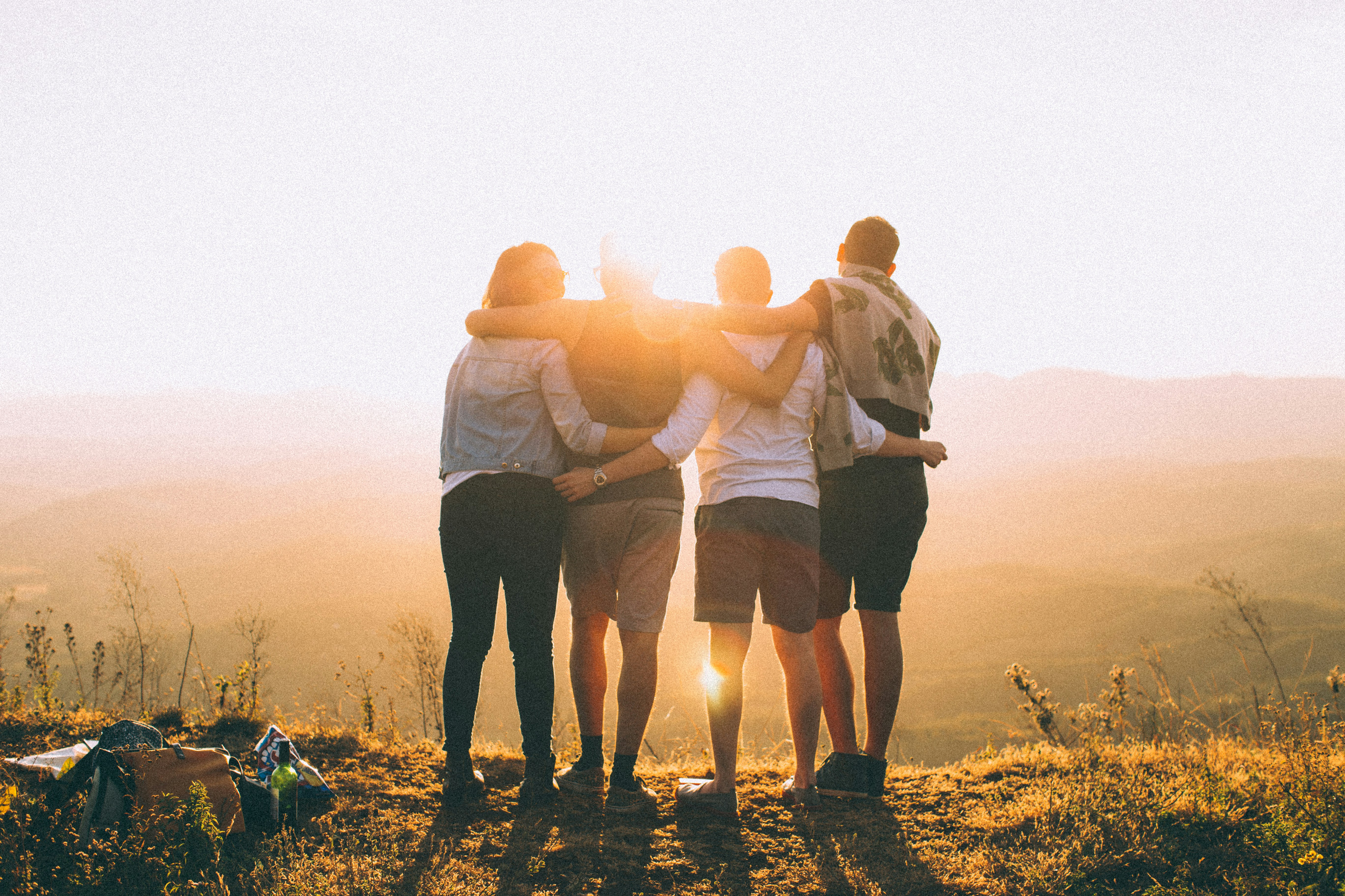 four young people huggin each other in from of the sunset